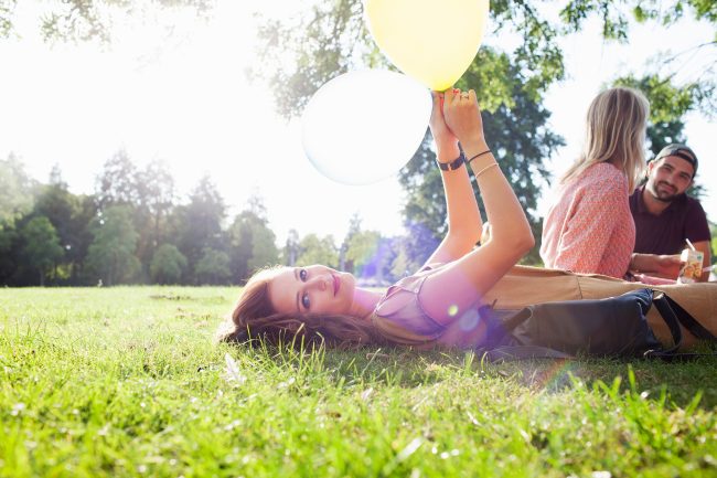 Portrait of young woman lying on grass with balloon at park party
